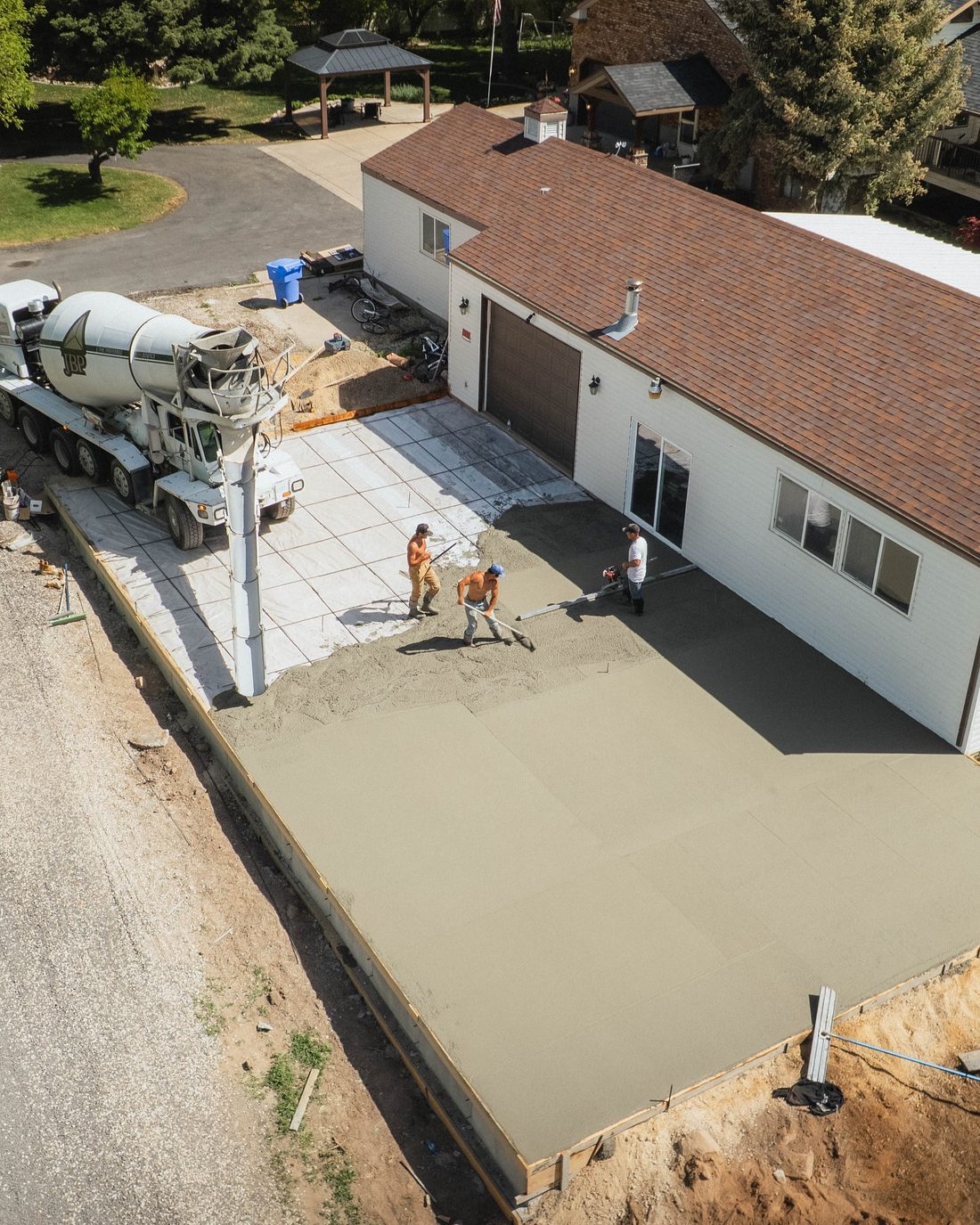 Crew pouring a large slab beside a garage, seen from above