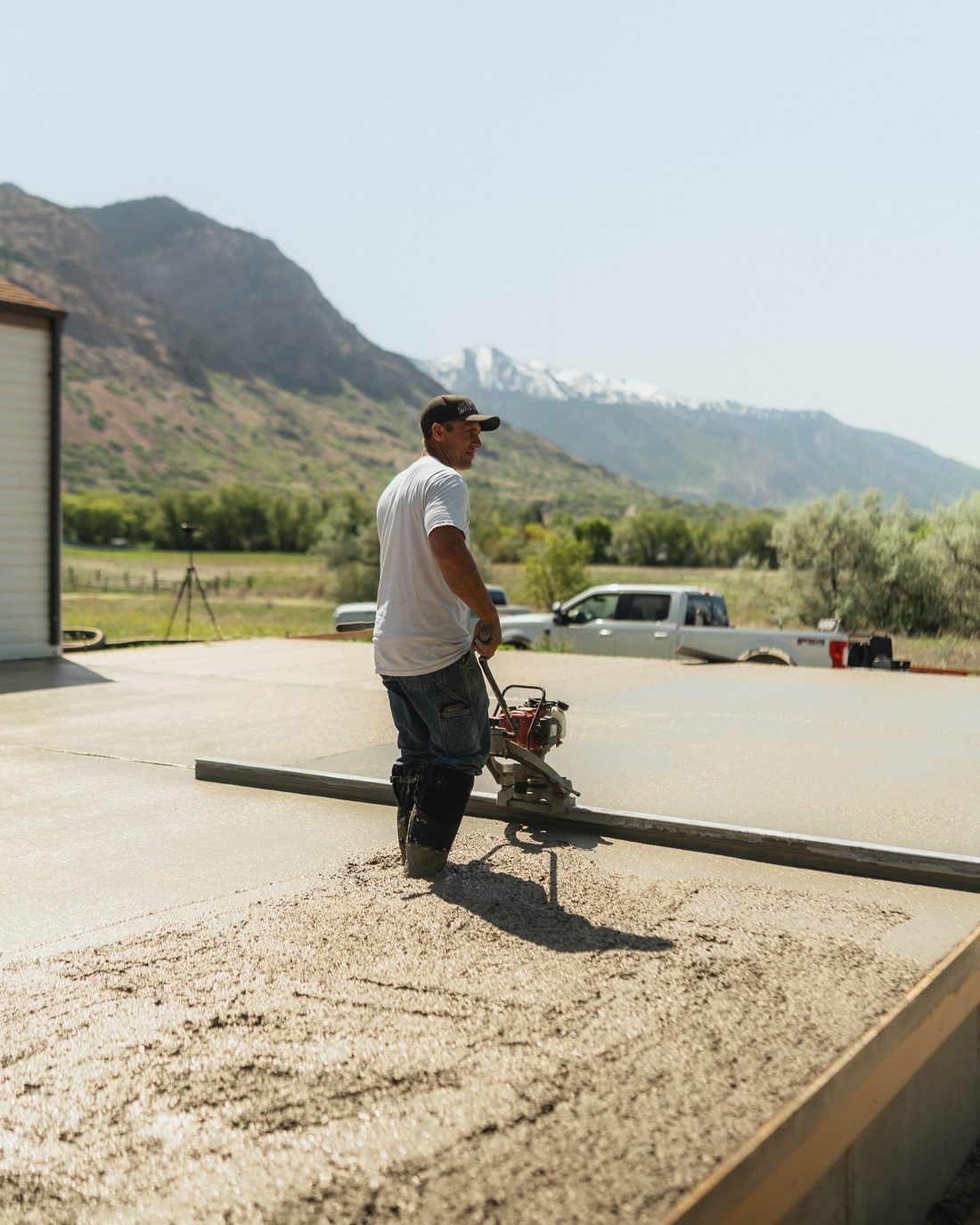 Finisher running a power screed across a fresh slab with mountains behind